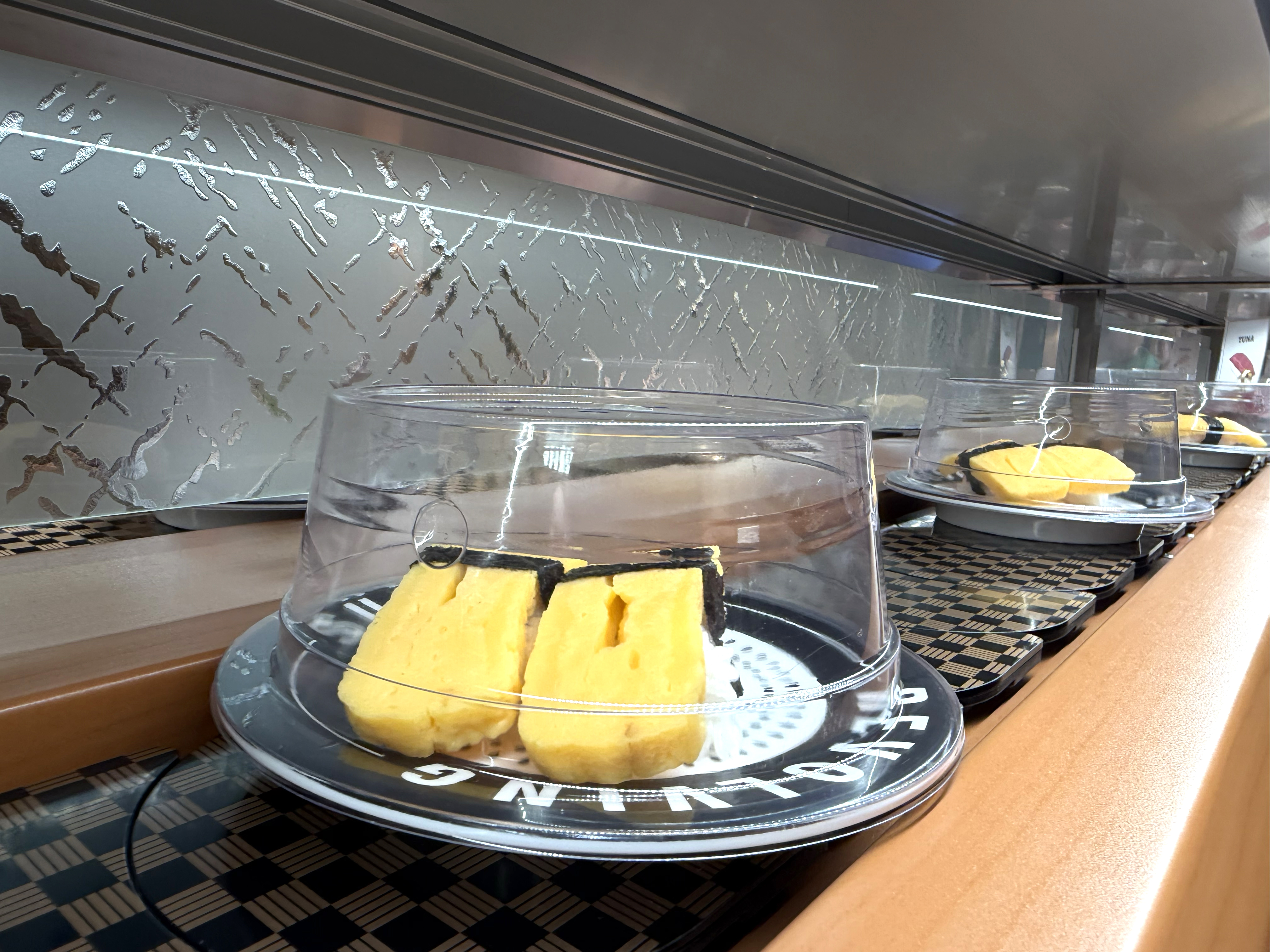 Freshly made tamago egg sushi plates rolling on the belt at Makoto Staten Island