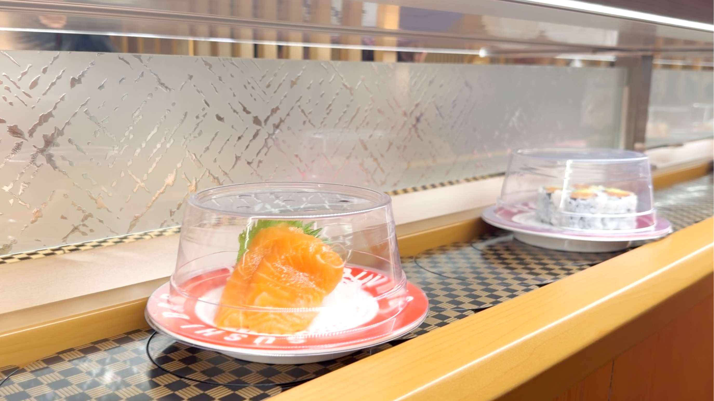 Fresh salmon sashimi on a red plate rolling along the belt at Makoto Staten Island
