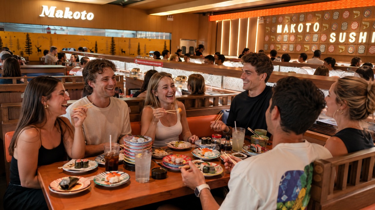Group of friends laughing and sharing plates of revolving sushi at Makoto Staten Island