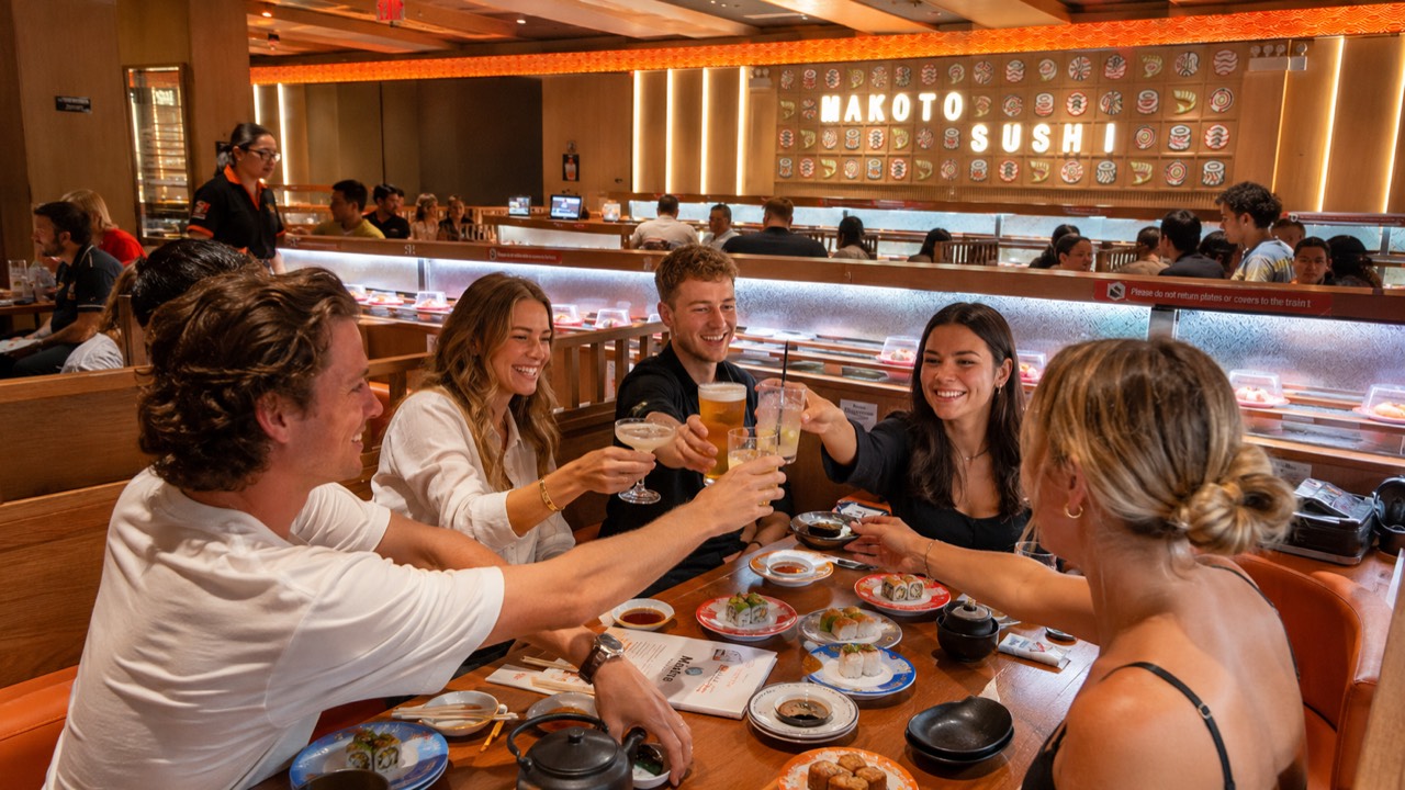 Friends toasting drinks together over sushi at Makoto revolving sushi bar in Staten Island