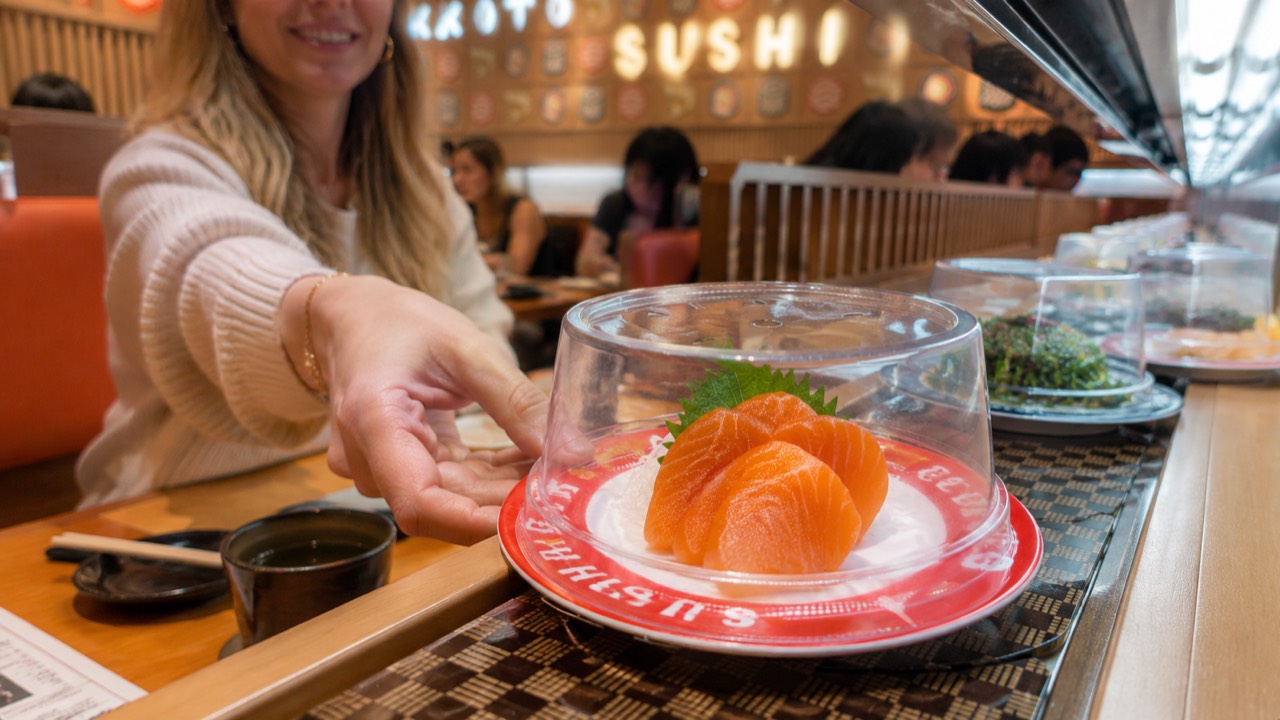Guest lifting the dome cover to take a salmon sashimi plate off the conveyor belt at Makoto Staten Island
