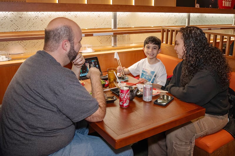 Family of three enjoying sushi and drinks in a booth at Makoto revolving sushi bar in Staten Island