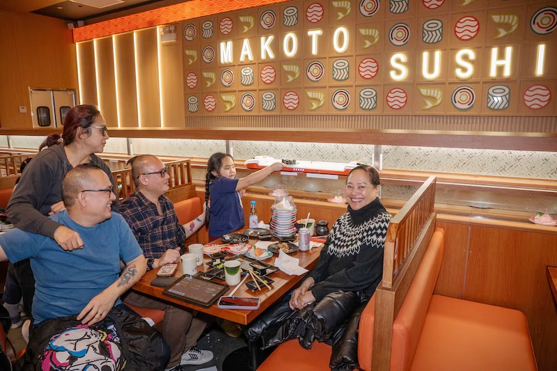 Family gathered around a booth table beneath the Makoto Sushi mural in Staten Island