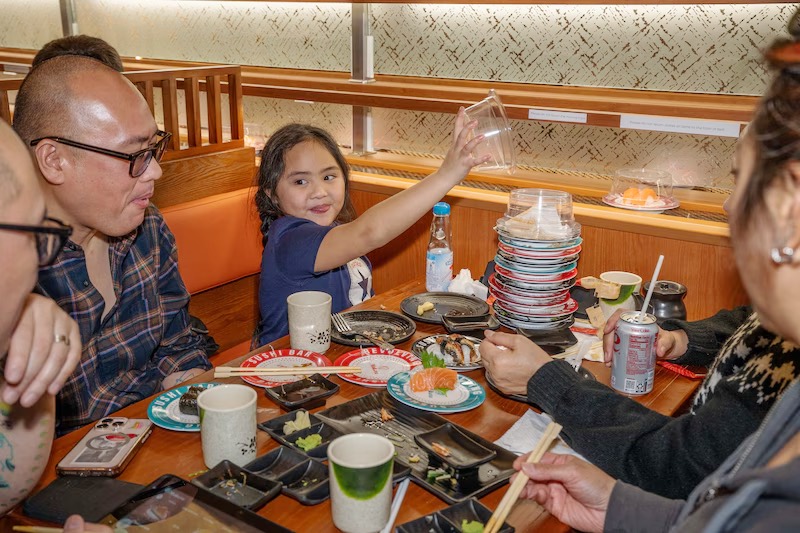 Family with a young girl and a stack of empty plates after a sushi feast at Makoto Staten Island