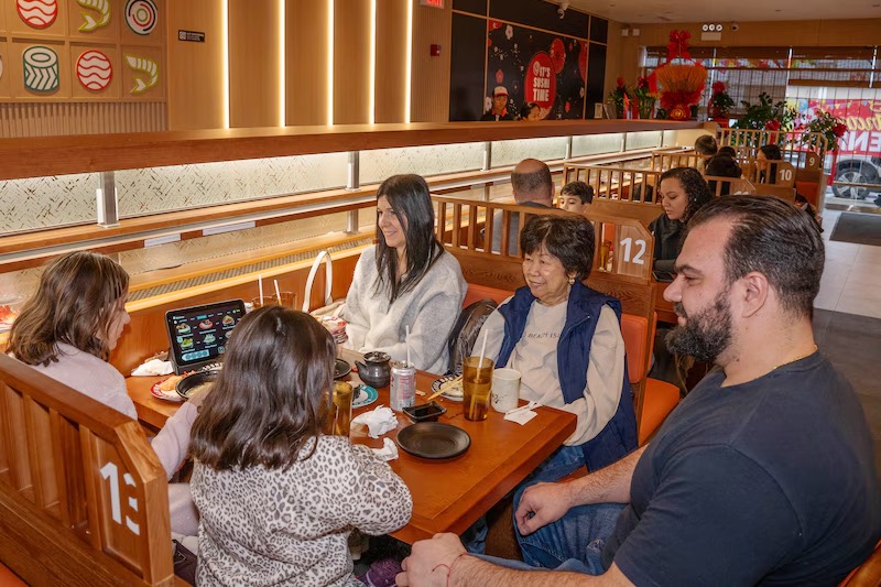 Friends enjoying drinks and sushi together in a booth at Makoto Staten Island